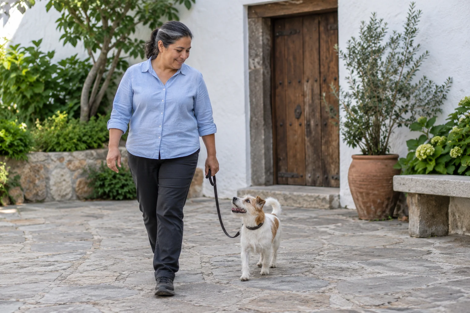 A caregiver walking beside a relaxed terrier in a bright courtyard